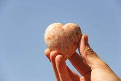 A hand holds a heart made of natural stone rhodochrosite against stock image A hand holds a heart made of natural stone rhodochrosite against stock image