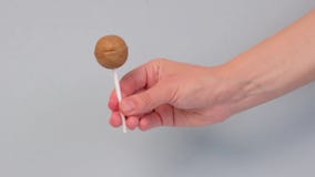 The hand holds a lollipop, caramel round on a stick and twirls it.