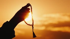 Hand holds rosary against the sky and the setting sun, sincere prayer and meditation