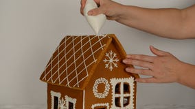 The hand-made eatable gingerbread house, adding by hand of icing on roof stock video The hand-made eatable gingerbread house, adding by hand of icing on roof stock video