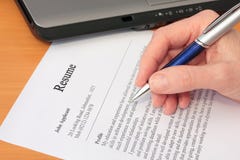 Hand with Pen Proofreading a Resume by Laptop