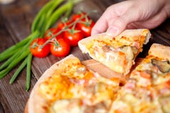 Hand picking tasty slice of pizza lying on wooden table