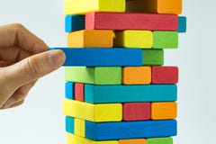Hand pulling colorful wooden block from the tower in as Risk or