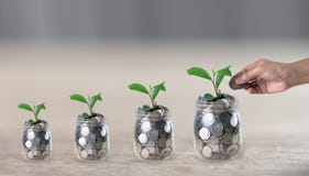 Hand putting a coin in a jar which a growing plant stock photos Hand putting a coin in a jar which a growing plant stock photos
