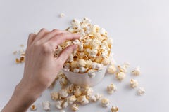 A hand is taking popcorn from a full paper bucket on a white background. Top view royalty free stock photo A hand is taking popcorn from a full paper bucket on a white background. Top view royalty free stock photo