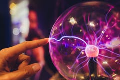 Hand touching a plasma ball with smooth magenta-blue flames.
