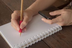 Hand van vrouw het schrijven notitieboekje en het kijken smartphone op houten stock afbeeldingen Hand van vrouw het schrijven notitieboekje en het kijken smartphone op houten stock afbeeldingen