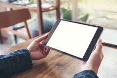 Handen die zwarte tabletpc met het lege witte Desktopscherm en laptop op houten lijst in koffie houden Royalty-vrije Stock Fotografie Handen die zwarte tabletpc met het lege witte Desktopscherm en laptop op houten lijst in koffie houden Royalty-vrije Stock Fotografie