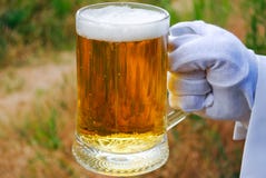 Handen för uppassare` s i en vit handske rymmer ett ölexponeringsglas mot bakgrunden av naturen royaltyfri foto Handen för uppassare` s i en vit handske rymmer ett ölexponeringsglas mot bakgrunden av naturen royaltyfri foto