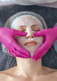 Hands of beautician in rubber gloves smoothes collagen hydrogel mask on woman face in a beauty salon