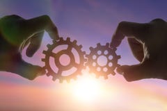 Hands businessman holding gears on the background of the sky in the sun, connecting the puzzle pieces. creation. mechanism. Stock Photo Hands businessman holding gears on the background of the sky in the sun, connecting the puzzle pieces. creation. mechanism. Stock Photo