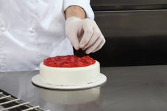 Hands pastry chef prepares a cake, cover with icing and decorate with strawberries, works on a stainless steel kitchen stock photography Hands pastry chef prepares a cake, cover with icing and decorate with strawberries, works on a stainless steel kitchen stock photography