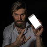 Handsome bearded man shows his phone with fascinating smile on a dark background. stock photo Handsome bearded man shows his phone with fascinating smile on a dark background. stock photo