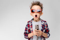 A handsome boy in a plaid shirt, gray shirt and jeans stands on a gray background. A boy wearing sunglasses. Red-haired stock image A handsome boy in a plaid shirt, gray shirt and jeans stands on a gray background. A boy wearing sunglasses. Red-haired stock image