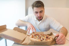 A handsome man stares at the pizza with a hungry look. The man is going to take a piece of pizza. royalty free stock photography A handsome man stares at the pizza with a hungry look. The man is going to take a piece of pizza. royalty free stock photography