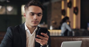 Handsome man using smartphone sitting in cafe or coworking office. Portrait of successful businessman entrepreneur stock footage Handsome man using smartphone sitting in cafe or coworking office. Portrait of successful businessman entrepreneur stock footage
