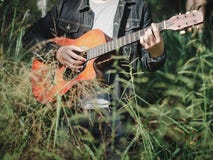 Handsome musician playing acoustic guitar at the grass field blur background. World music day. music and instrument concept stock image Handsome musician playing acoustic guitar at the grass field blur background. World music day. music and instrument concept stock image