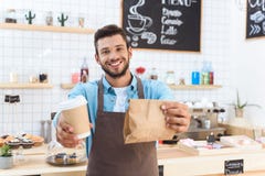 handsome smiling young barista holding coffee to go in paper cup and take away food