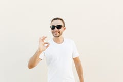 Handsome young man over orange wall wearing sunglasses doing happy thumbs up gesture with hand. Approving expression looking at th stock images Handsome young man over orange wall wearing sunglasses doing happy thumbs up gesture with hand. Approving expression looking at th stock images