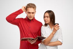 A handsome young man in a red shirt looks at the book thoughtfully scratching head. stock photos A handsome young man in a red shirt looks at the book thoughtfully scratching head. stock photos
