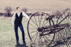A handsome young man in a waistcoat, black trousers and a white shirt. Is standing next to a haymaking machine in the field Royalty Free Stock Image A handsome young man in a waistcoat, black trousers and a white shirt. Is standing next to a haymaking machine in the field Royalty Free Stock Image