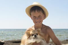 Happy 8 Year Old Boy Hugging His Dog Pomeranian Shpitz At The Seashore Against A Blue Sky. Stock Image