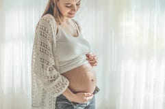 Happy Attractive pregnant woman standing near the window and holding her belly stock photography Happy Attractive pregnant woman standing near the window and holding her belly stock photography