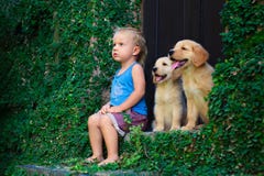 Happy baby boy sitting with two golden labrador retriever puppies