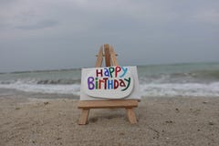 Happy Birthday message carved and painted on a stone over an easel with beach background