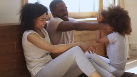 Happy black parents and child daughter tickling sit on floor