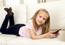 Happy blond little girl on home sofa using internet app on mobile phone royalty free stock photos Happy blond little girl on home sofa using internet app on mobile phone royalty free stock photos