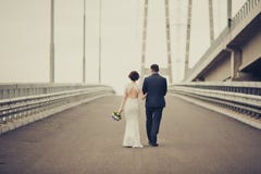 Happy bride and groom celebrating wedding day. Married couple going away on bridge. Long family life road concept. Toned Stock Photo Happy bride and groom celebrating wedding day. Married couple going away on bridge. Long family life road concept. Toned Stock Photo
