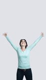 A happy brunette girl in a mint-colored jumper stands against the gray background The young woman raised her hands up smiles royalty free stock image A happy brunette girl in a mint-colored jumper stands against the gray background The young woman raised her hands up smiles royalty free stock image