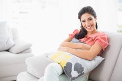 Happy brunette sitting on her sofa smiling at camera Royalty Free Stock Images Happy brunette sitting on her sofa smiling at camera Royalty Free Stock Images