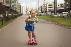 Happy child girl riding a scooter in the summer on the road stock photo Happy child girl riding a scooter in the summer on the road stock photo