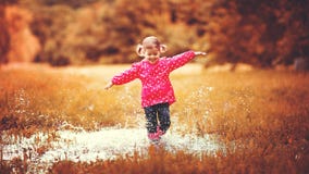 Happy child girl running and jumping in puddles after rain