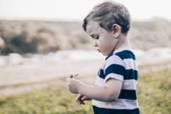 Happy child, little boy looks down, pensive look and holding in hands the growths outdoors. Space for Text. Retro toned. Summer stock photography Happy child, little boy looks down, pensive look and holding in hands the growths outdoors. Space for Text. Retro toned. Summer stock photography