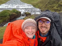 Happy couple adventure travelers man and woman in raincoats with waterfall behind. Freedom traveling and active lifestyle concept stock photography Happy couple adventure travelers man and woman in raincoats with waterfall behind. Freedom traveling and active lifestyle concept stock photography