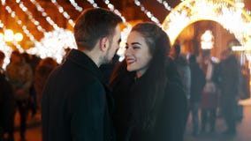 Happy couple kissing on the crowded street, date against the background of lights from garlands, New Year Christmas