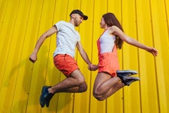Happy couple in love jumping against yellow wall. Young hipsters stock photos Happy couple in love jumping against yellow wall. Young hipsters stock photos