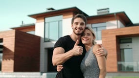 Happy couple making thumbs up near luxury house. Excited family smiling outside stock video footage Happy couple making thumbs up near luxury house. Excited family smiling outside stock video footage
