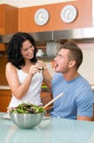 Happy Couple Playfully Eating Salad At Kitchen Stock Photography
