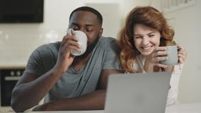 Happy couple talking at open kitchen. Smiling man and woman looking at laptop. stock footage Happy couple talking at open kitchen. Smiling man and woman looking at laptop. stock footage