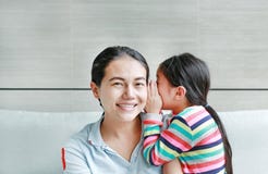 Happy cute little Asian child girl whispering a secret to her young mothers ear at home. Family and relationships concept stock image Happy cute little Asian child girl whispering a secret to her young mothers ear at home. Family and relationships concept stock image