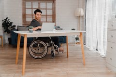 Happy Disabled Asian Man Sitting In A Wheelchair And Working With Computer At Home, The Concept Of Technologies For The Stock Photo