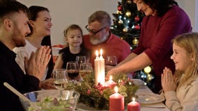 Happy family celebrating holiday together, sitting around decorated round table. Mother serving dinner. Living room with stock footage Happy family celebrating holiday together, sitting around decorated round table. Mother serving dinner. Living room with stock footage