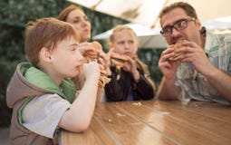 Happy family eating burgers sitting at a table in a cafe stock photo Happy family eating burgers sitting at a table in a cafe stock photo