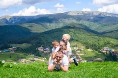 Happy family: joyful father, mother and two sons are lying on the green grass against the background of the forest, mountains and royalty free stock photography Happy family: joyful father, mother and two sons are lying on the green grass against the background of the forest, mountains and royalty free stock photography