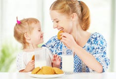 Happy family mother and baby daughter girl at breakfast: biscuits with milk