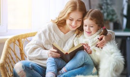 Happy family mother reads book to child to daughter by window stock photo Happy family mother reads book to child to daughter by window stock photo